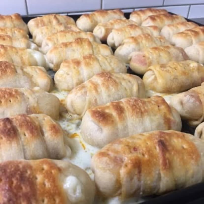 Many golden-brown baked pizza rolls, some with melted cheese oozing out, on a baking sheet.