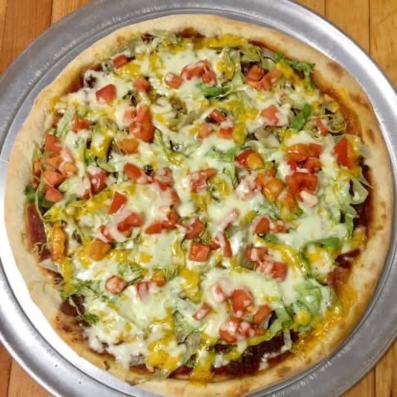 A Pizza Village V taco pizza, topped with melted cheese, shredded lettuce, diced tomatoes, and mustard.