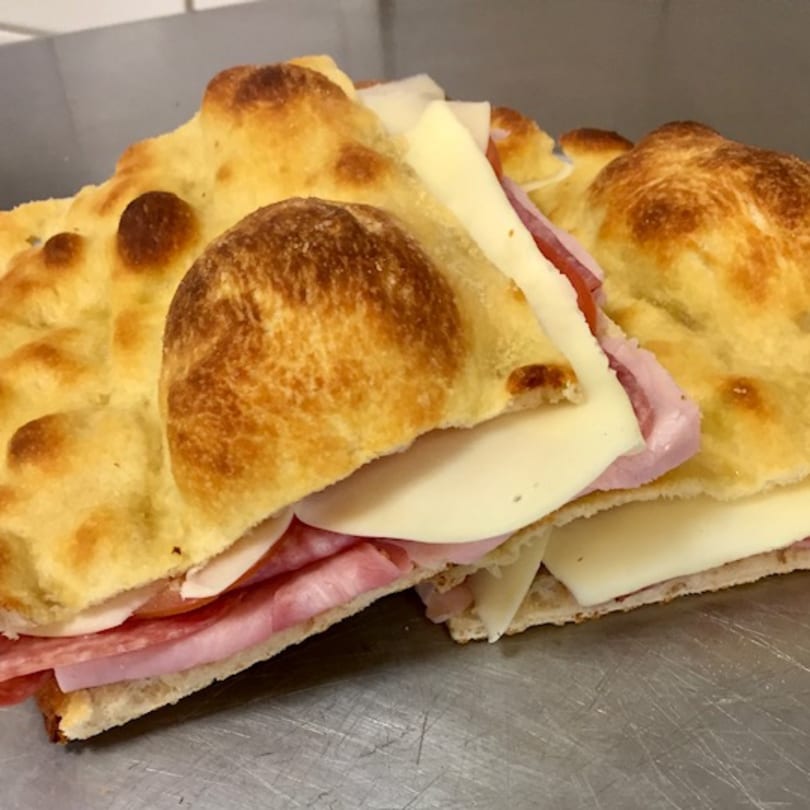 Two focaccia sandwiches filled with ham, salami, and cheese on a metal surface.