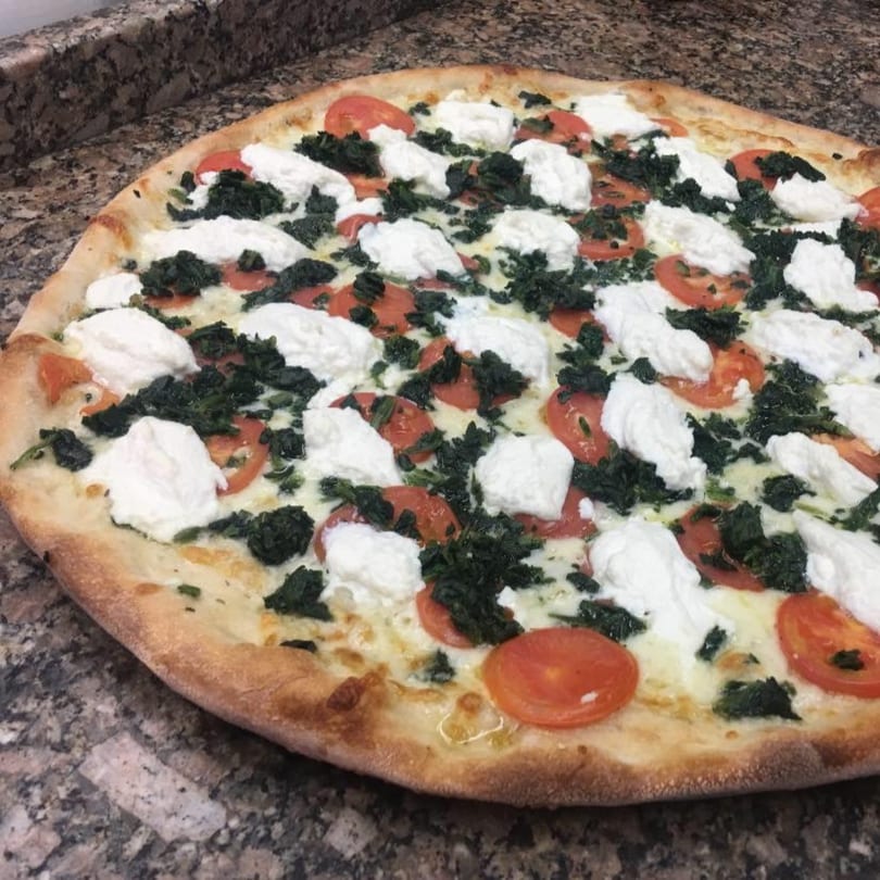 A Pizza Village V pizza with white ricotta cheese, red tomatoes, and green spinach on a marble counter.
