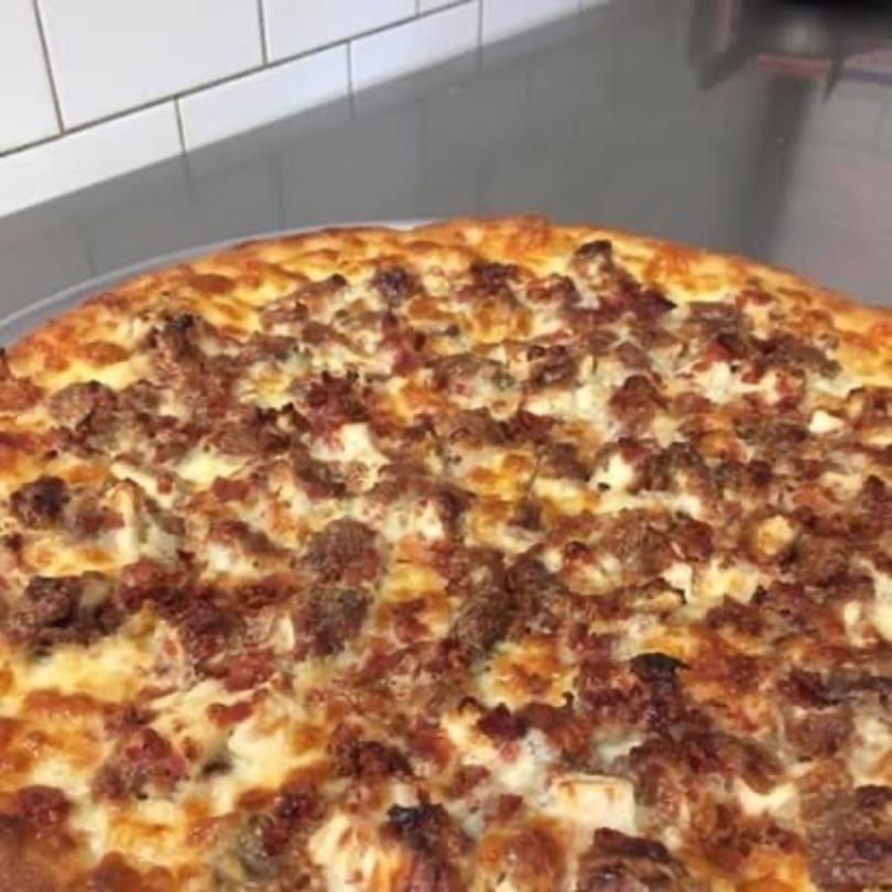 Close-up of a Pizza Village V pizza with a golden crust and generous meat toppings.