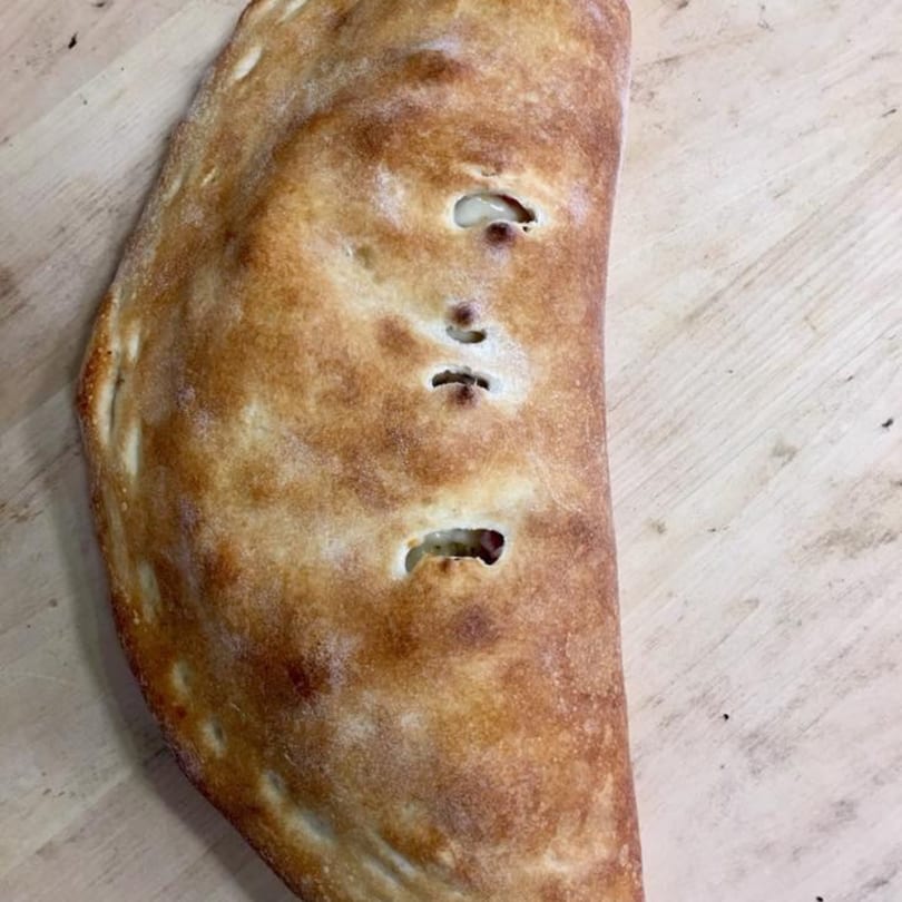 A golden-brown calzone with small vents on a light wooden surface, from Pizza Village V.