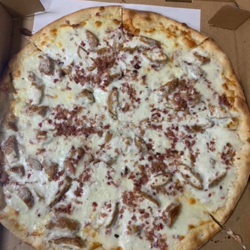 A white pizza from Pizza Village V, topped with chicken and bacon, in a delivery box.