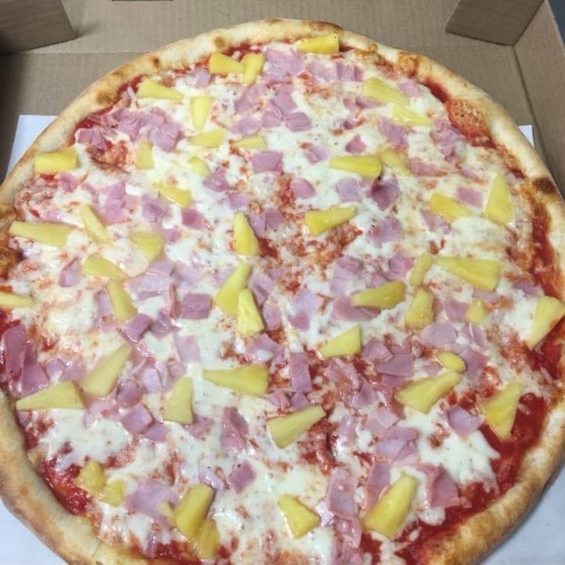 A whole Hawaiian pizza with ham and pineapple in a cardboard box from Pizza Village V.