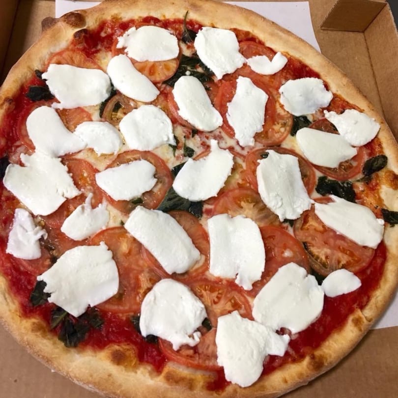 A Pizza Village V Margherita pizza with fresh mozzarella, sliced tomatoes, and basil in a box.