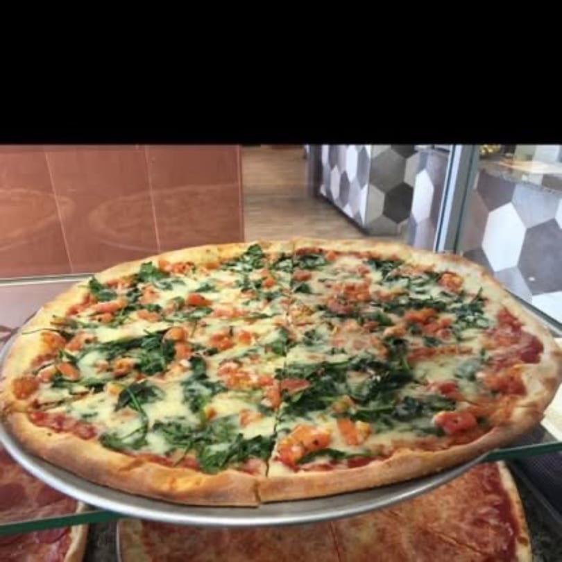 A large, round pizza with white cheese, green spinach, and orange diced tomatoes on a metal tray.