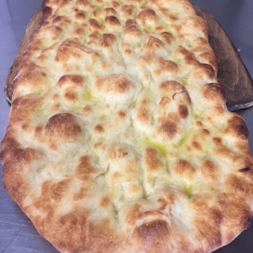 Golden brown focaccia bread with dimples of olive oil, on a wooden peel.