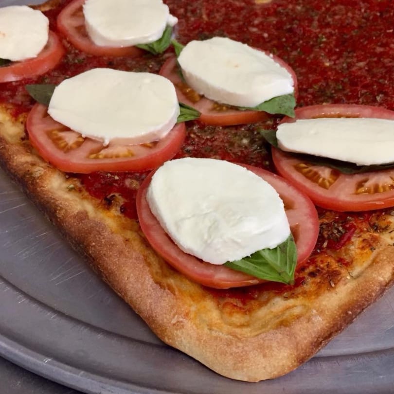 Close-up of a square pizza with tomato sauce, fresh mozzarella, basil, and sliced tomatoes.