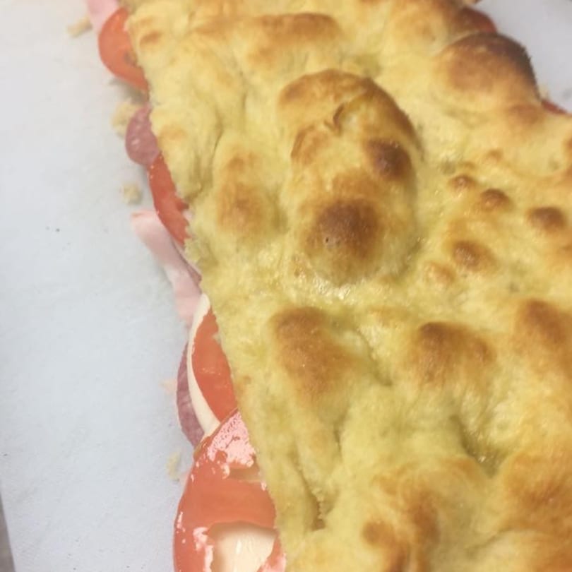 Close-up of a focaccia sandwich with salami, cheese, and tomatoes from Pizza Village V.