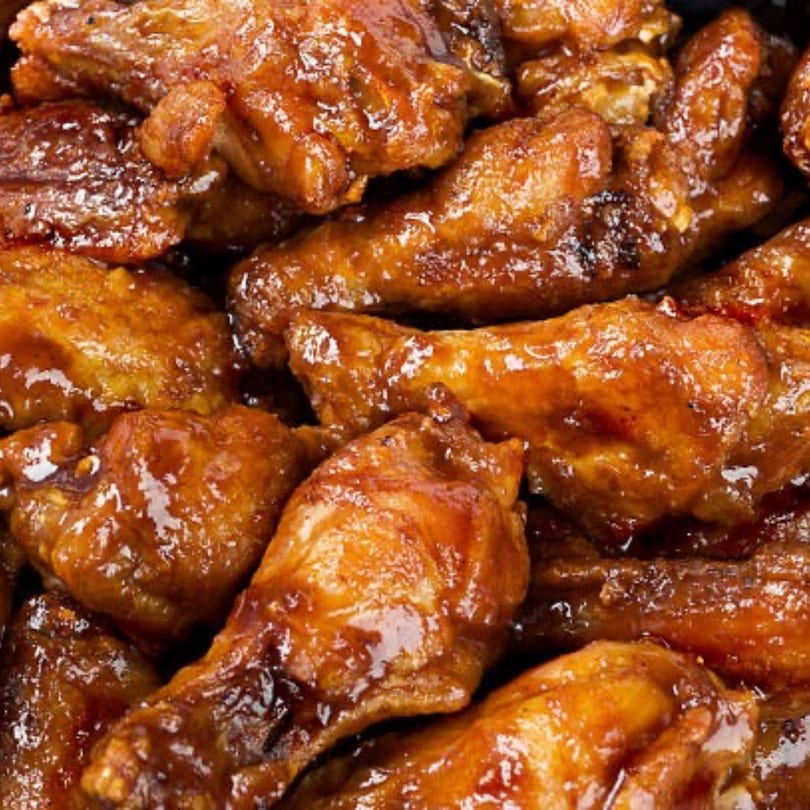Close-up of a pile of glistening, saucy chicken wings from Pizza Village V.